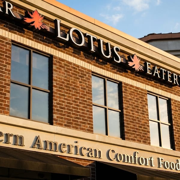 Exterior of Lotus Eatery, a brick building with large windows and signs for "Modern American Comfort Food".