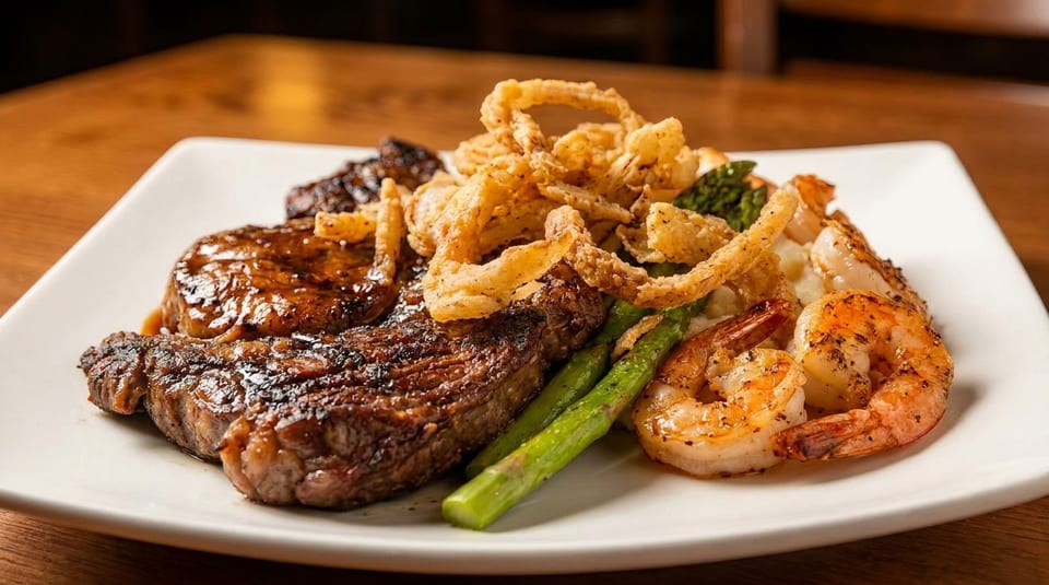 Grilled steak, fried onion rings, asparagus, and shrimp on a white rectangular plate.