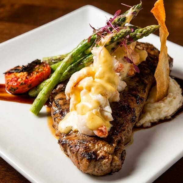 Grilled steak topped with lobster and hollandaise, served with asparagus, tomato, and mashed potatoes.