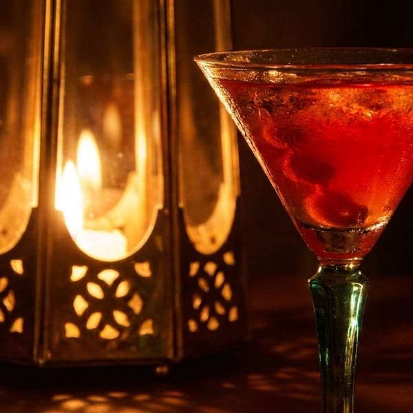 A red cocktail in a martini glass next to a glowing lantern with intricate cutouts.