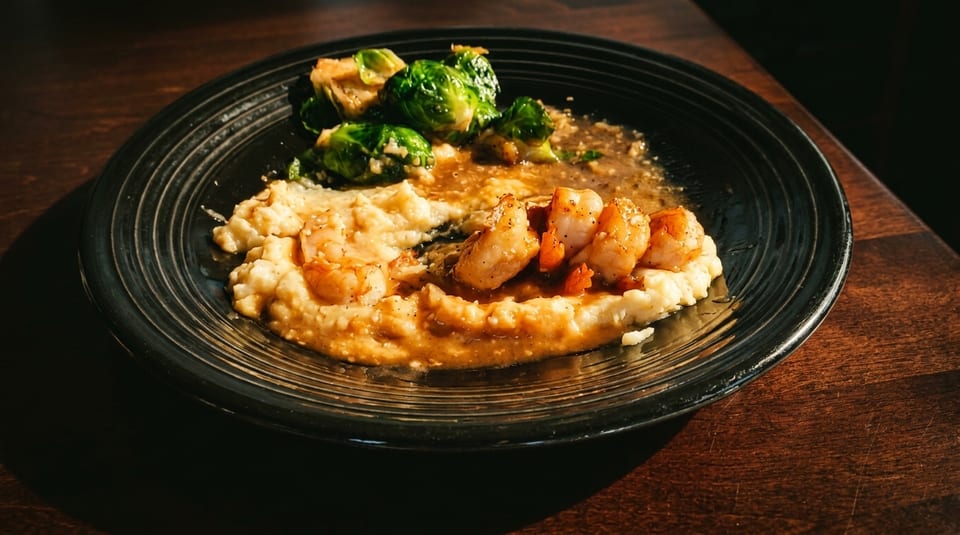 Shrimp and grits with gravy and Brussels sprouts on a black plate.
